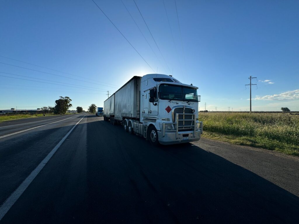 Silver semi truck driving on an open highway under a clear blue sky