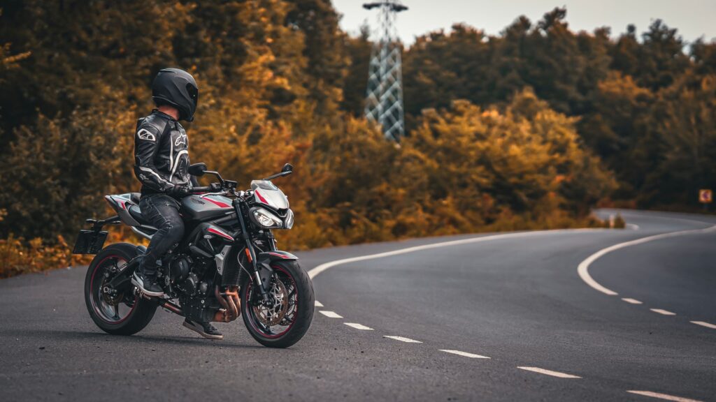 Motorcycle rider in a helmet and riding gear on a quiet road lined with autumn trees